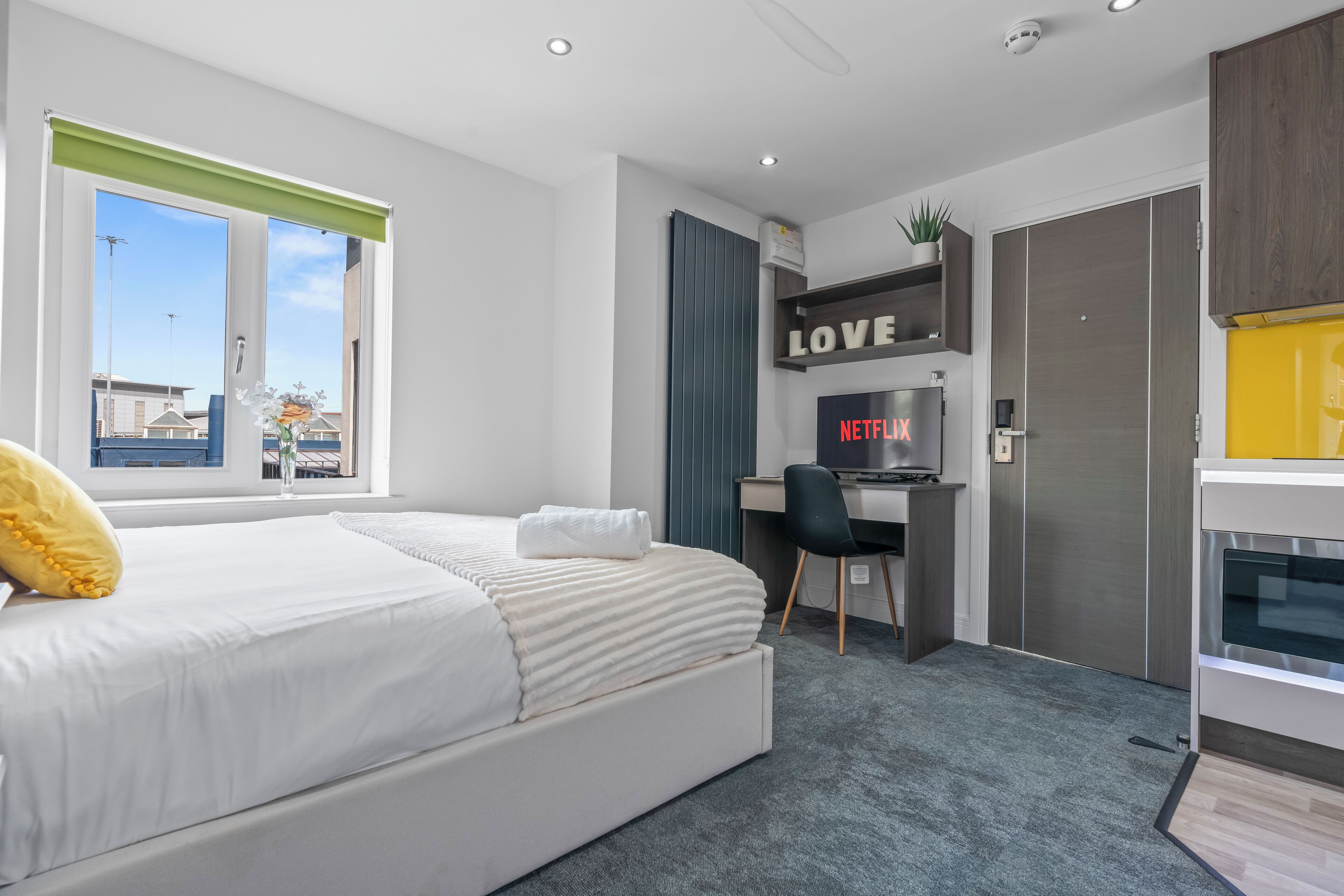 A modern hotel room with a bed, desk, and wardrobe.
