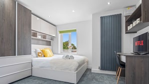 A modern bedroom with a bed, a desk, and a window. - New House Serviced Apartments (Coventry)