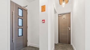 A hallway with a wooden door, a fire alarm, and a door with the number 101. - New House Serviced Apartments (Coventry)