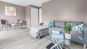 A modern living room with a grey sofa, two armchairs, a glass coffee table, and a potted plant. - Modern 4-Bed Close to Jaguar Whitley & City C… (Coventry)