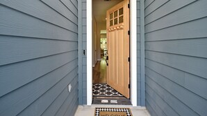 A hallway with a wooden door and a welcome mat at the entrance. - Downtown Tomball-Built in 2025, King Bed, Sleeps 6 (Tomball)