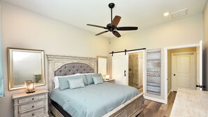 A bedroom with a bed, nightstands, a ceiling fan, and a door leading to another room. - Downtown Tomball-Built in 2025, King Bed, Sleeps 6 (Tomball)