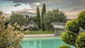 A swimming pool with a lounge chair and umbrella, surrounded by greenery and tall trees. - Le Logis des Écuries **** - Charming rooms with swimming pool - Côte Roannaise (Renaison)
