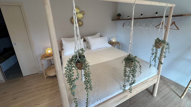 A bed with a wooden frame, hanging macramé plants, and a bedside table with a lamp. - Le Logis des Écuries **** - Charming rooms with swimming pool - Côte Roannaise (Renaison)
