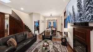 A spacious living room with a leather sofa, a coffee table, and a fireplace. - Top 1% - 4BR/HotTub/Sauna/Massage Chairs (Revelstoke)