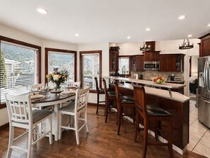 A modern kitchen with wooden cabinets, a central island, and a dining area with white chairs.