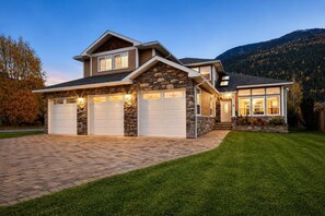 Une maison à deux étages avec une façade en pierre, deux garages attenants et une pelouse bien entretenue.
