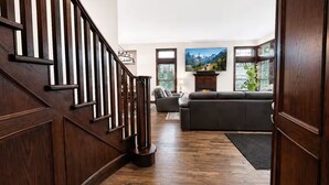 A wooden staircase leading to a living room with a fireplace, a large TV, and a sofa. - Top 1% - 4BR/HotTub/Sauna/Massage Chairs (Revelstoke)