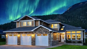 A two-story house with a stone facade, two garage doors, and a well-lit entrance. - Top 1% - 4BR/HotTub/Sauna/Massage Chairs (Revelstoke)