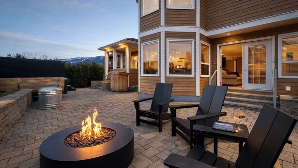 A patio with a fire pit, outdoor seating, and a view of a multi-story building with large windows. - Top 1% - 4BR/HotTub/Sauna/Massage Chairs (Revelstoke)