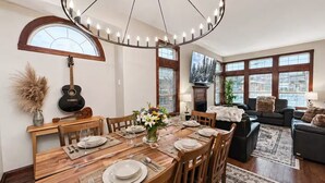A dining area with a wooden table set for six, a guitar, and a chandelier. - Top 1% - 4BR/HotTub/Sauna/Massage Chairs (Revelstoke)