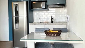 Een moderne keuken met een roestvrijstalen koelkast, een magnetron en een gasfornuis. Er is een glazen eettafel met twee stoelen.
