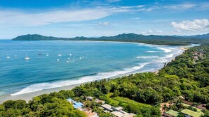 Vista aérea de una zona costera con playa, barcos y abundante vegetación.