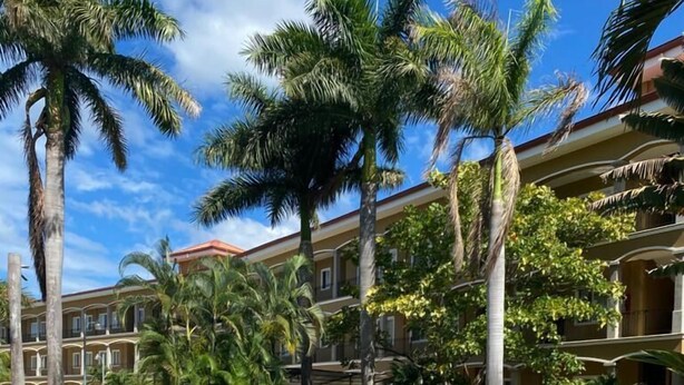 Una piscina rodeada de palmeras y un edificio de varios pisos con balcones.