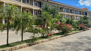 Un hotel de varios pisos con balcones, palmeras y plantas en flor.