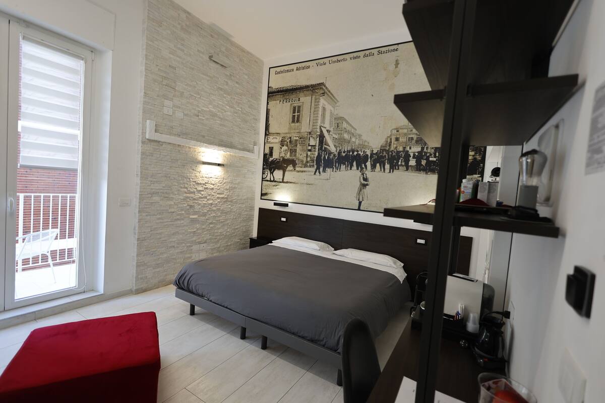 Un dormitorio moderno con una cama grande, un banco rojo, una pared de piedra y un cartel con un paisaje urbano.