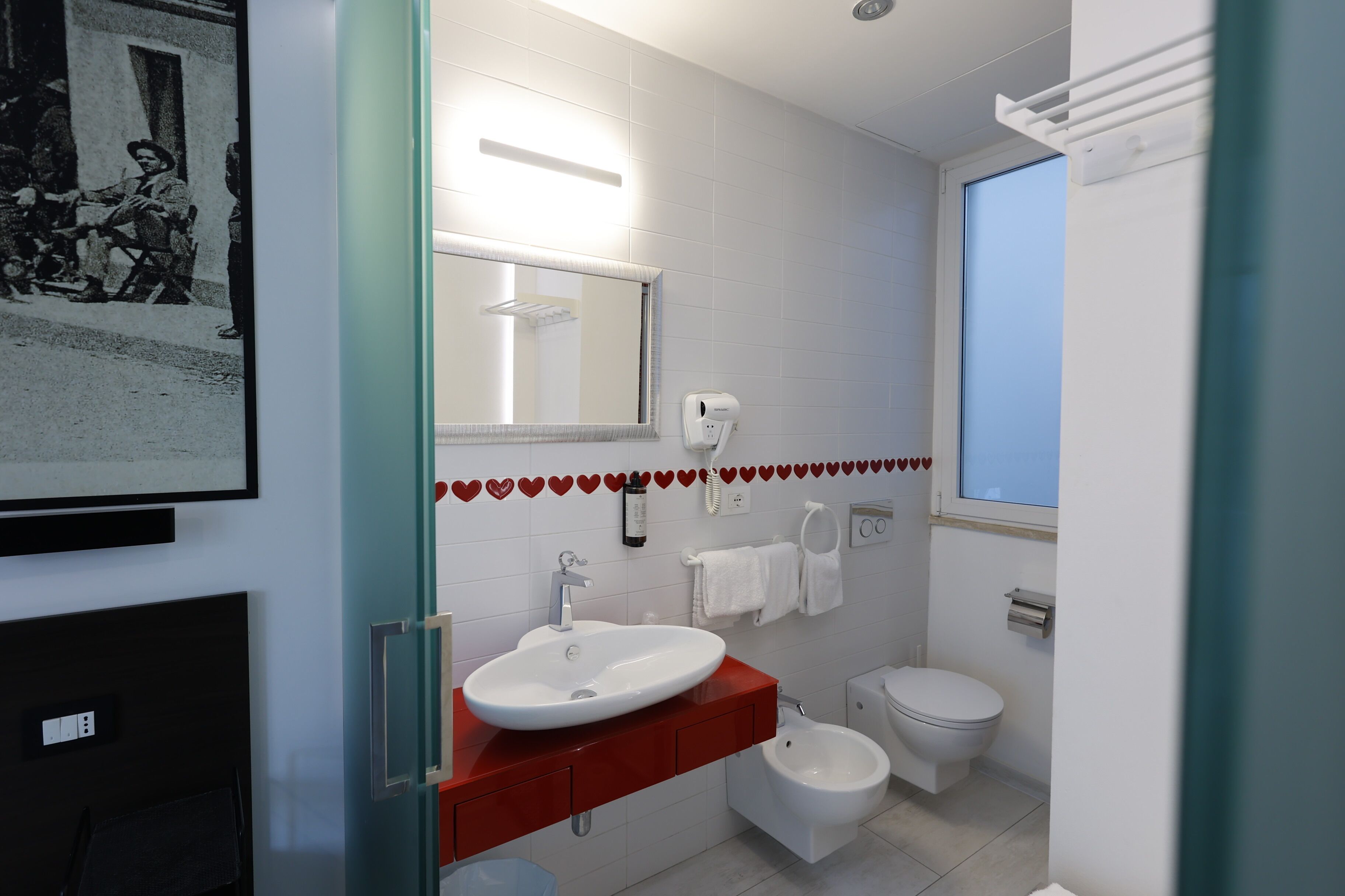 A modern bathroom with a white sink, red vanity, bidet, and a large mirror.