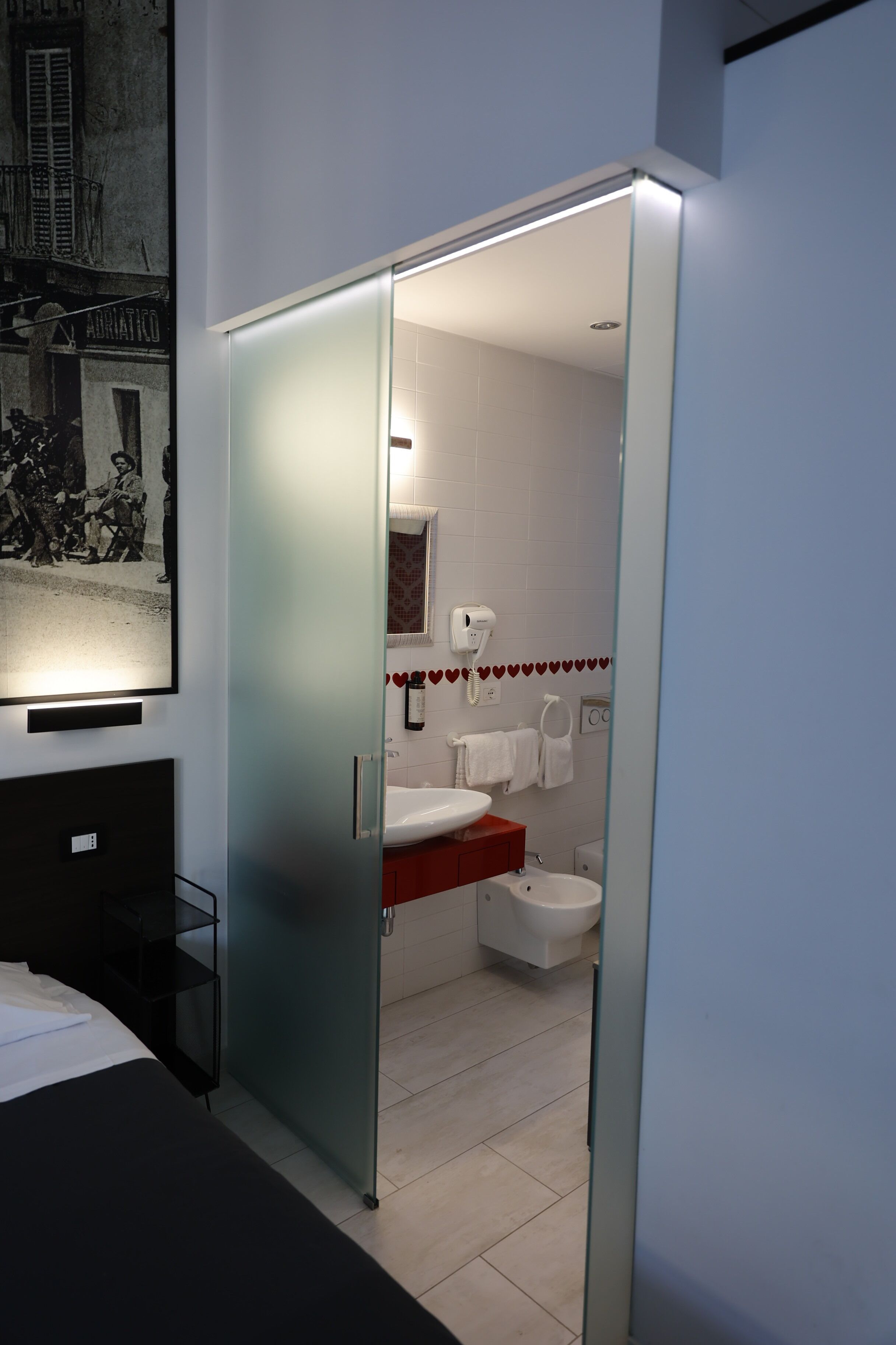 Et moderne badeværelse med glasdør, hvid vask, toilet og spejl.