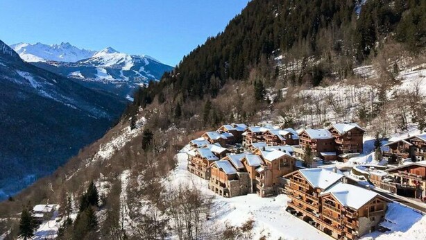 Une station de montagne enneigée, avec des chalets en bois et une vue dégagée sur les sommets enneigés en arrière-plan.