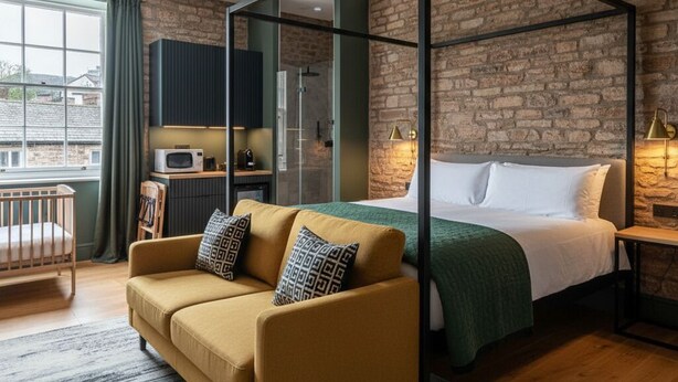 A modern bedroom with a four-poster bed, a sofa, a crib, and a kitchenette. - The Civic Hall - Wayth Hotels (Hebden Bridge)