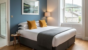 A bedroom with a large bed, a bedside table, a lamp, and a window with a view of buildings. - The Civic Hall - Wayth Hotels (Hebden Bridge)