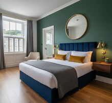 Un dormitorio con una cama grande, un espejo redondo, una mesita de noche con una lámpara y vistas a un paisaje verde a través de una ventana.