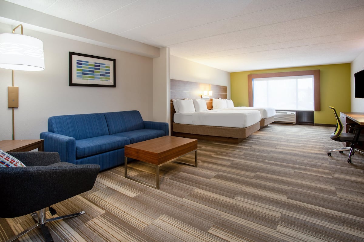 Une chambre d’hôtel avec un lit, un canapé bleu, une table basse en bois, un bureau avec une chaise et une grande fenêtre.