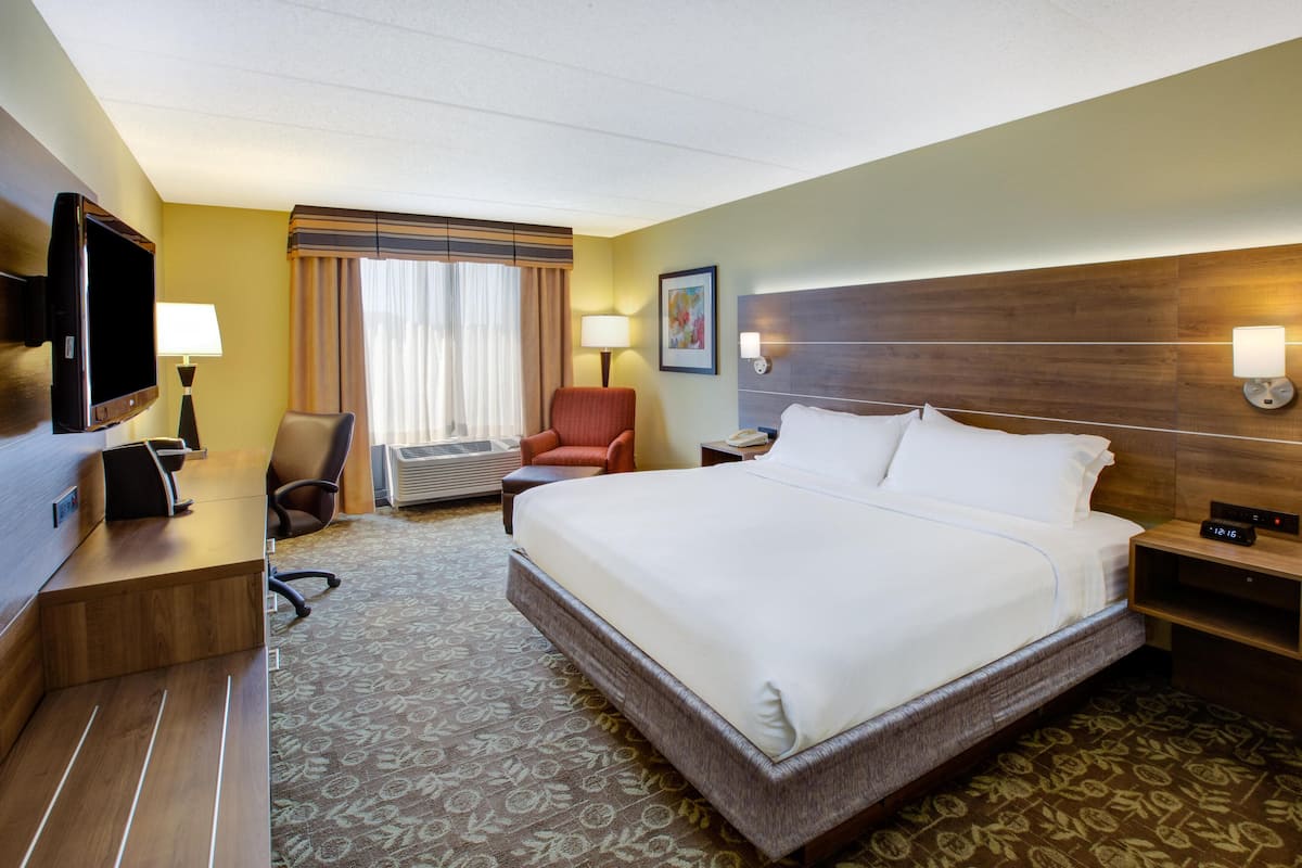 Une chambre d’hôtel avec un grand lit, un bureau doté d’un téléviseur à écran plat, une chaise, une table de chevet avec une lampe et une fenêtre avec des rideaux.