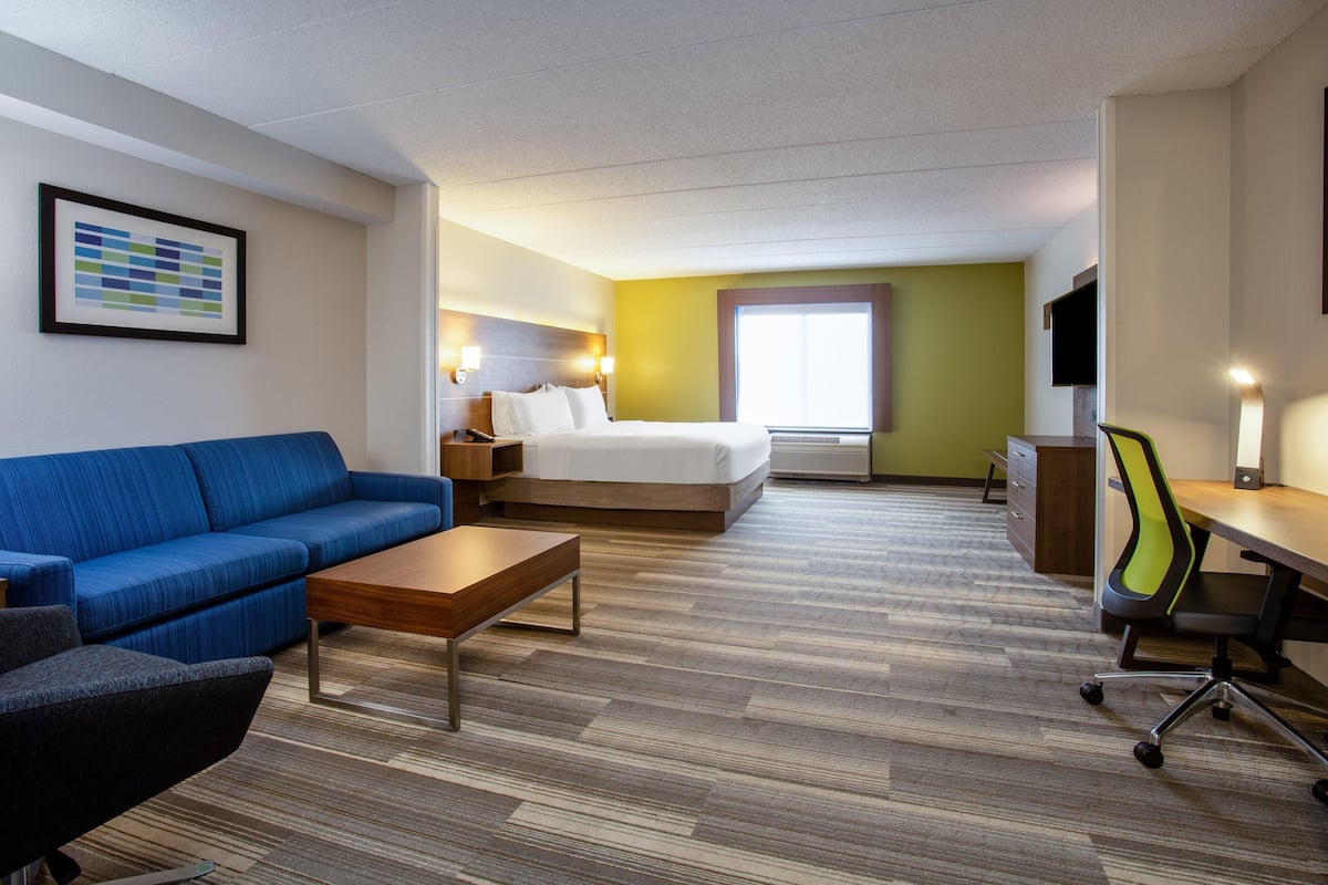 Une chambre d’hôtel avec un lit, un canapé bleu, une table basse en bois, un bureau avec une chaise et un téléviseur.