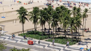 A beach with palm trees, a road, and mountains in the background. - Atlantica Prime Copacabana Ocean View (Rio de Janeiro)