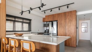 A modern kitchen with a central island, wooden chairs, and a large window with blinds. - Atlantica Prime Copacabana Ocean View (Rio de Janeiro)