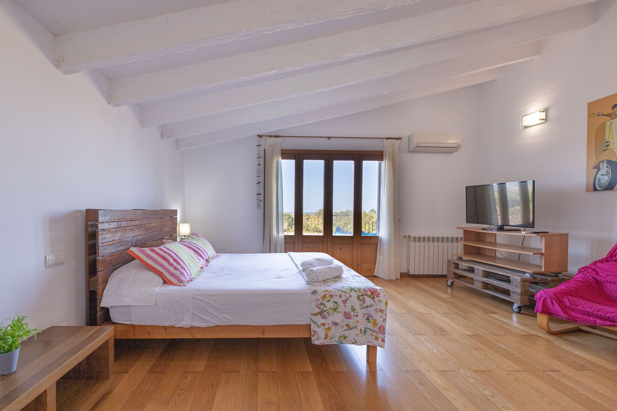 A bedroom with a wooden bed, a TV, a bench, and a window with curtains.