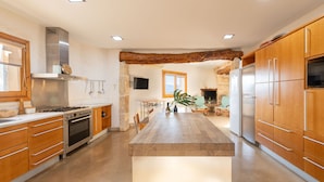 A modern kitchen with wooden cabinets, a central island, stainless steel appliances, and a stone accent wall.