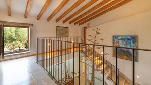 A modern interior with a wooden ceiling, a glass railing staircase, and artwork on the walls.