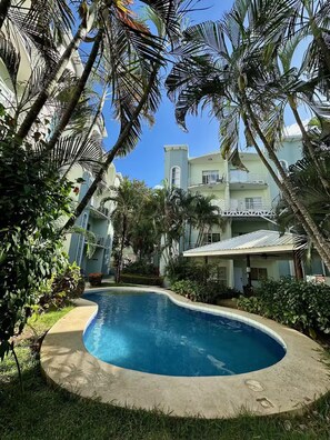 A swimming pool surrounded by lush greenery and a multi-story building with balconies.