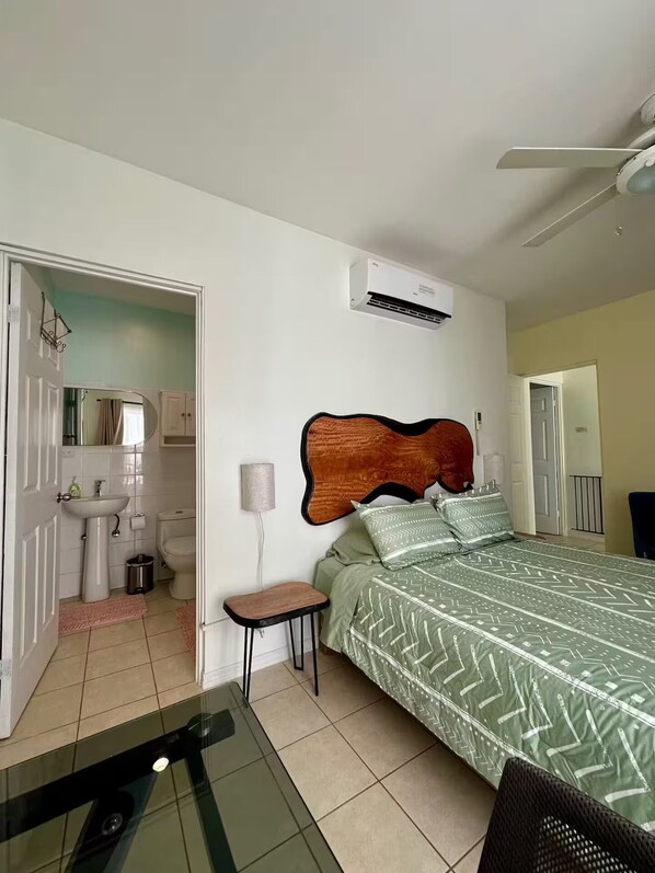 A bedroom with a bed, bedside table, and a nightstand. There is a bathroom visible through an open door.