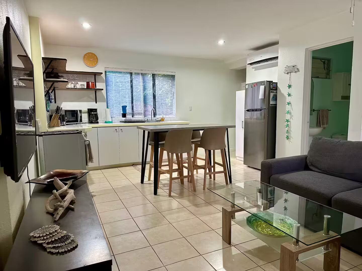 A modern kitchen with a dining area, a glass coffee table, and a sofa.