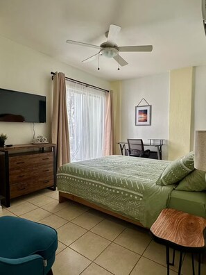 Ein Schlafzimmer mit einem Bett, einem Schreibtisch, einem Sessel, einem Fernseher und einem Deckenventilator.