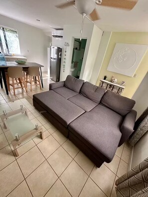 A modern living room with a grey sofa, a glass coffee table, and a dining area with a table and chairs.