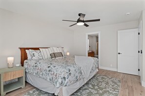 A bedroom with a bed, bedside table, nightstand, ceiling fan, and a door.