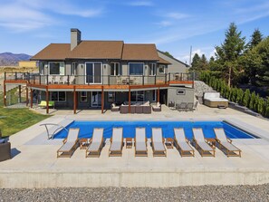 A two-story house with a large backyard pool, outdoor furniture, and a hot tub.