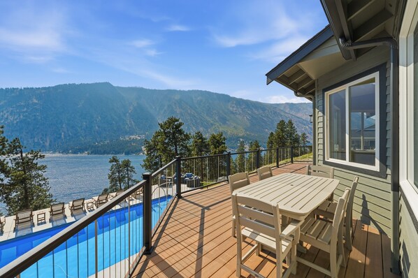 A deck with a pool, outdoor furniture, and a view of a lake and mountains.