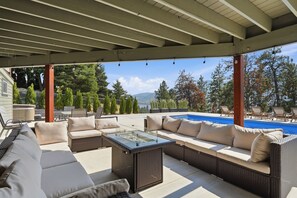 A covered outdoor seating area with a pool, wicker furniture, and a view of trees and mountains.