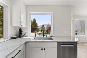 A modern kitchen with a large window, a coffee maker, and a view of a deck and trees.