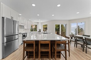 A modern kitchen with a large island, stainless steel appliances, and a dining area with wooden chairs.