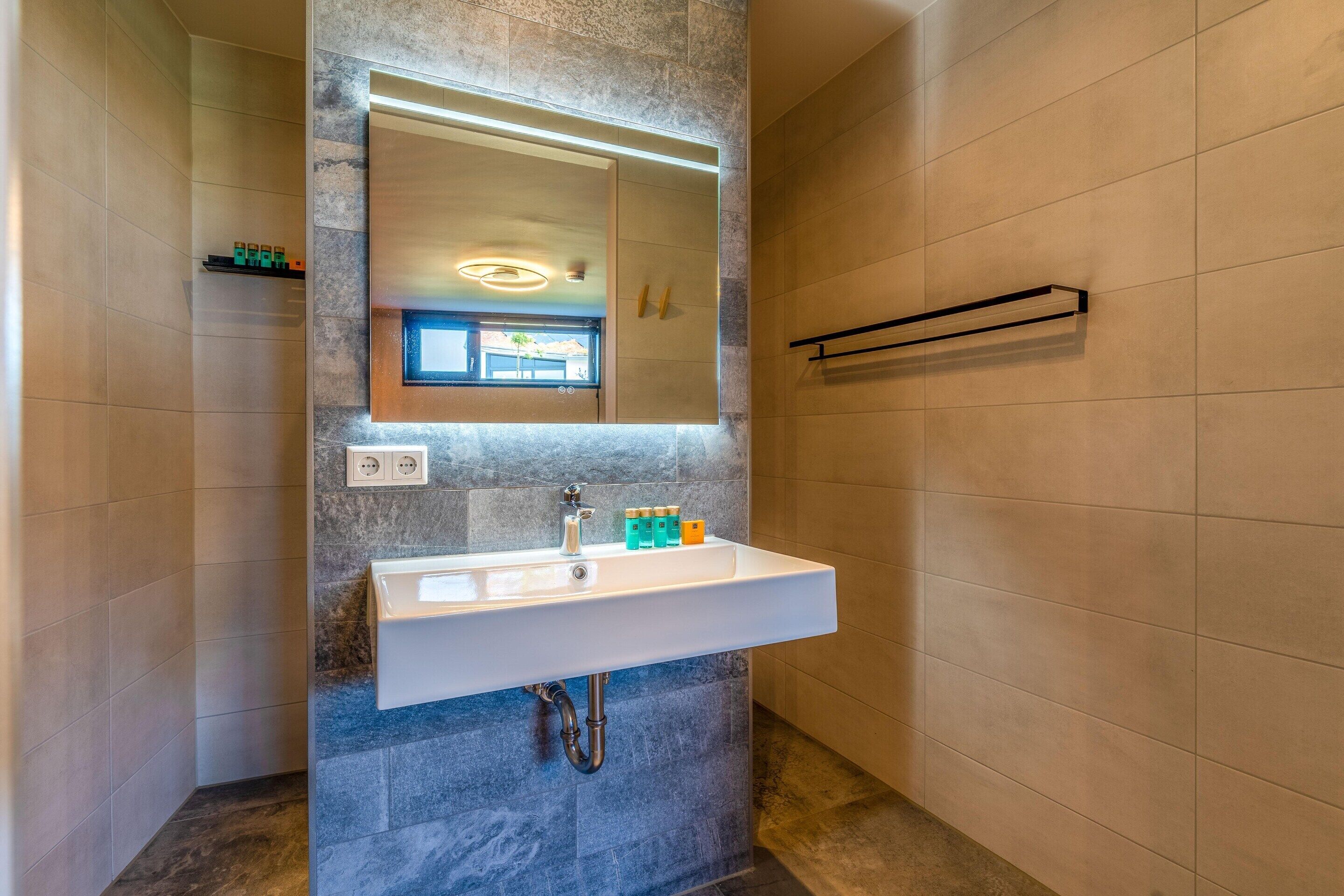 Un baño moderno con lavamanos integrado, un espejo grande y un perchero para toallas.