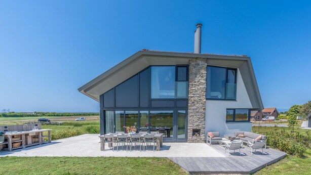 Une maison moderne dotée d’une grande terrasse, d’un espace salon extérieur et offrant une vue sur la campagne.