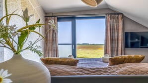 Une chambre avec un grand lit, une vue sur un champ par la fenêtre et un téléviseur à écran plat fixé au mur.