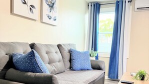 Un canapé gris agrémenté de coussins à motifs bleus, une petite table avec une plante et des œuvres d’art accrochées au mur.