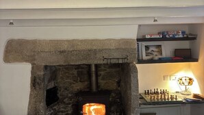 Une cheminée en pierre avec un feu visible, un jeu d’échecs et des étagères remplies de livres et d’objets décoratifs.